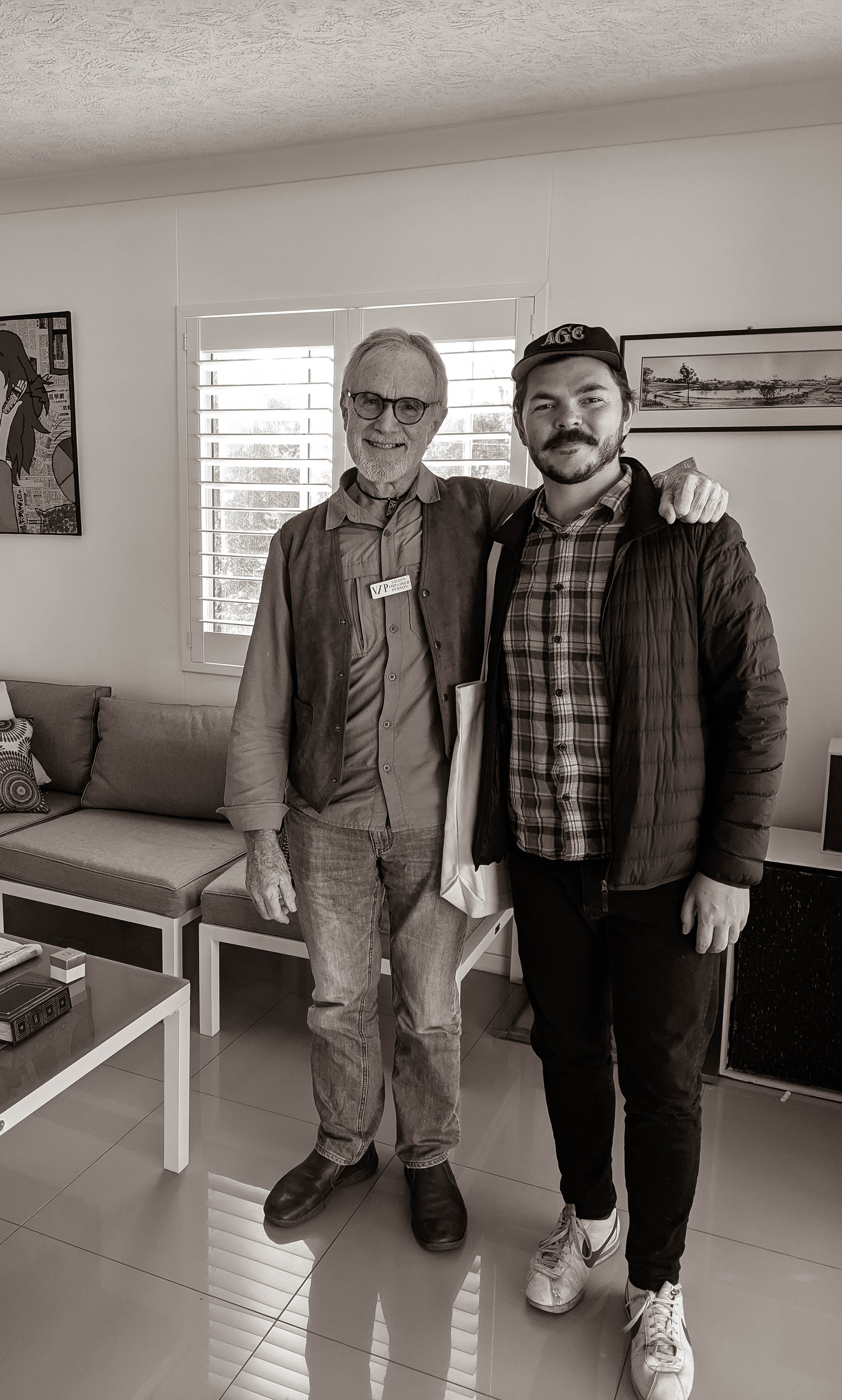 Black and white photo of Peter Vance standing in room with friend, both smiling at camera