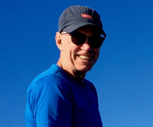 Gary Myers looking at camera wearing navy blue cap and blue shirt against a blue sky