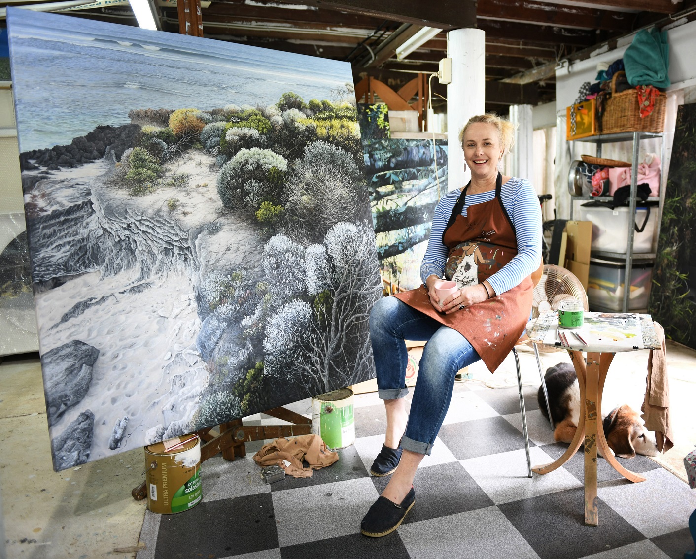 Naomi White sitting in studio in front of her painting with dog nearby on the floor