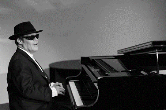 Dr Jeff Usher playing on piano with hat on and wearing a suit