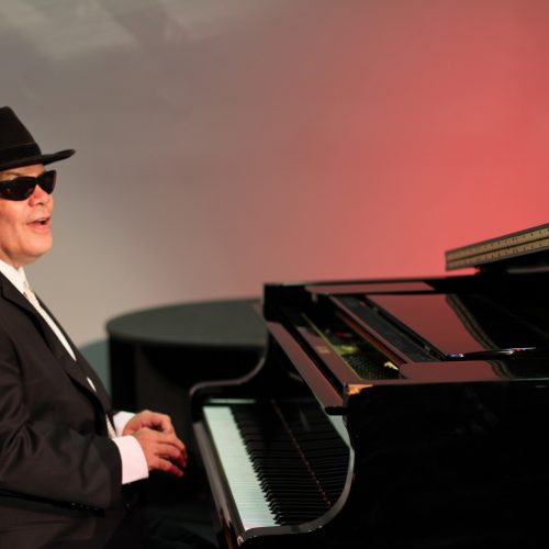 Photo of Jeff Usher sitting down at a grand piano wearing a suit