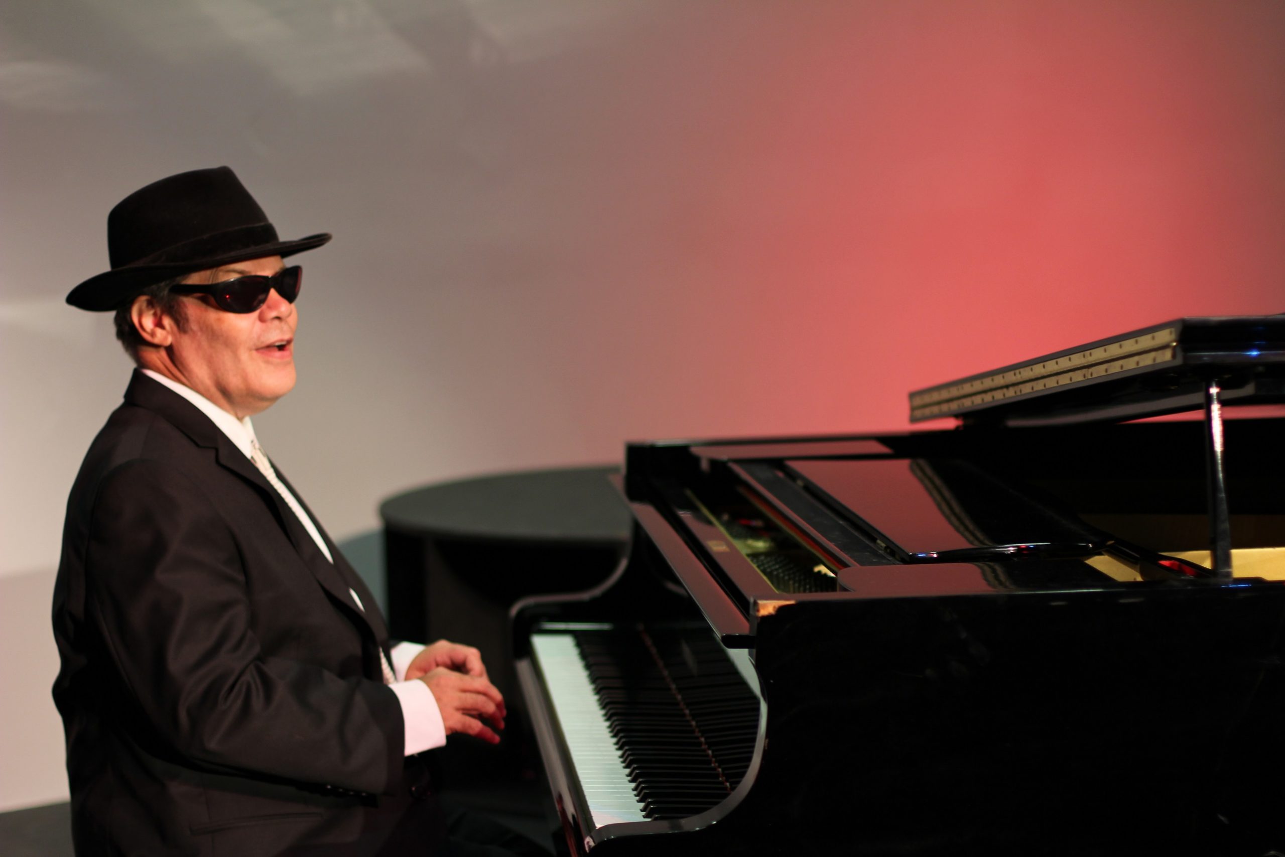 Photo of Jeff Usher sitting down at a grand piano wearing a suit