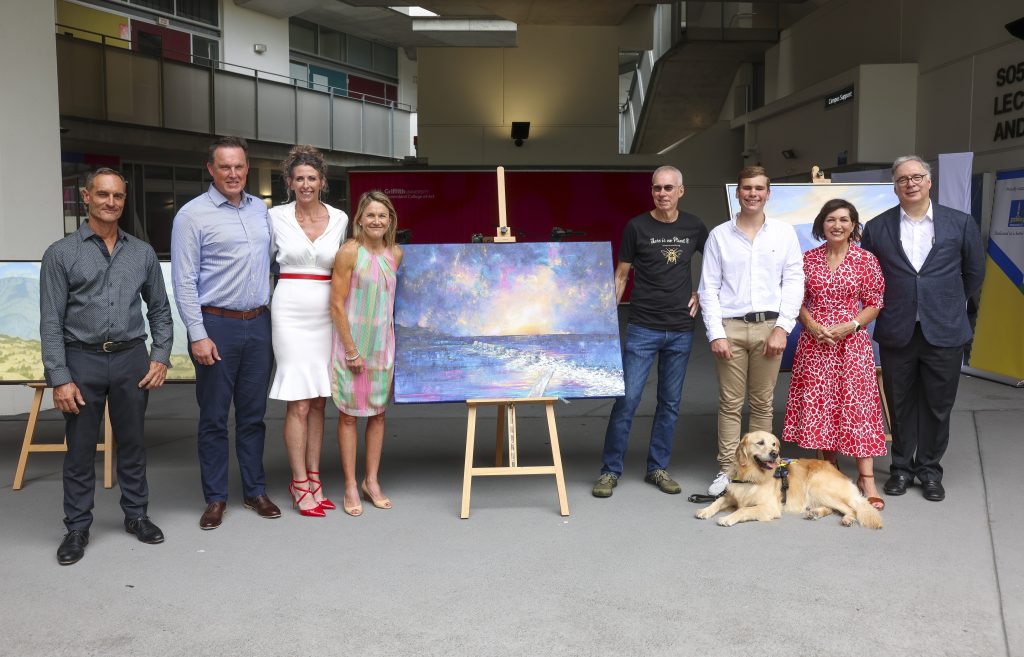 Group photo, left to right Robert Brownhall, Lorin Nicholson OAM, Tracie Eaton, Katie Kelly OAM PLY, painting in the centre, Gary Myers, Oliver Fanshawe with Seeing Eye Dog Sadie in front, Hon Leeanne Enoch and Professor Mark Radford.
